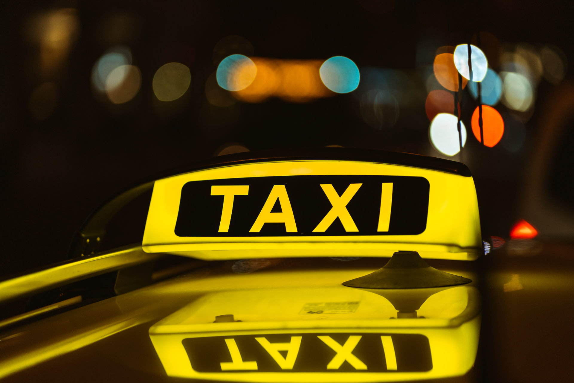 Black and yellow sign of Taxi at night placed on top of a car