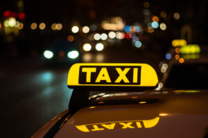 Yellow and black sign of Taxi placed on top of a car at night